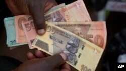 FILE — A currency trader holds Zimbabwean dollar notes on the streets of Harare, Zimbabwe, June, 9, 2022. 