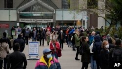 People queue in a line, at right, to go for coronavirus booster jabs at St Thomas' Hospital, in London, Monday, Dec. 13, 2021. 