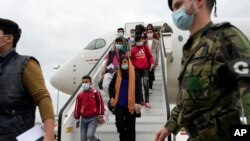 Afghan music students, faculty members and their families walk off an airplane at Lisbon military airport, Monday, Dec. 13, 2021. A group of 273 students, faculty members and their families from the Afghanistan National Institute of Music arrived Monday i