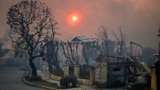 The sun is seen behind smoke above charred structures and vehicles after the passage of the Palisades Fire in Pacific Palisades, California, Jan. 8, 2025. 