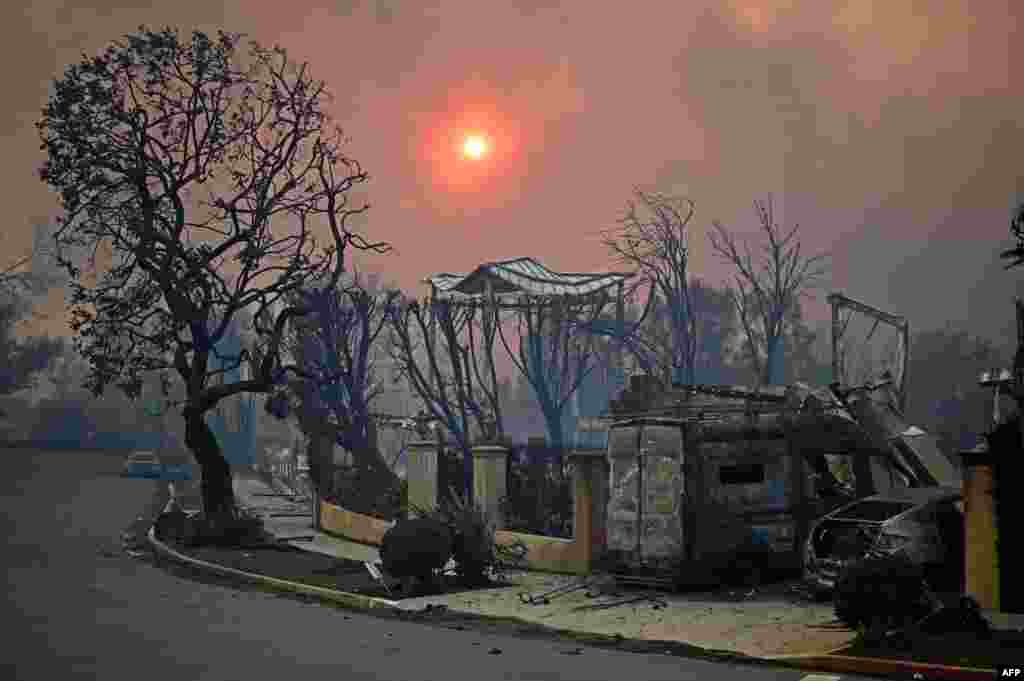 The sun is seen behind smoke above charred structures and vehicles after the Palisades Fire raged in Pacific Palisades, California, Jan. 8, 2025.&nbsp;At least five people have been killed in wildfires rampaging around Los Angeles, officials said, with firefighters overwhelmed by the speed and ferocity of multiple blazes.