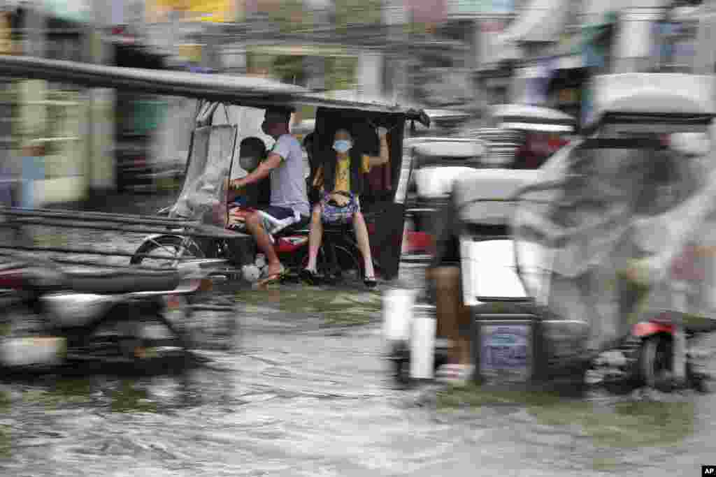 Residents wearing masks to prevent the spread of the coronavirus ride motorcycles as they negotiate a flooded road due to Typhoon Molave in Pampanga province, northern Philippines on Monday, Oct. 26, 2020. A fast moving typhoon has forced thousands of vil