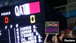 A supporter of Nepal's women's basketball team holds up a sign alongside a scoreboard showing names of Qatar's women's basketball team members after they failed to show up for their scheduled game at the 17th Asian Games in Incheon, South Korea, Sept. 25, 2014.