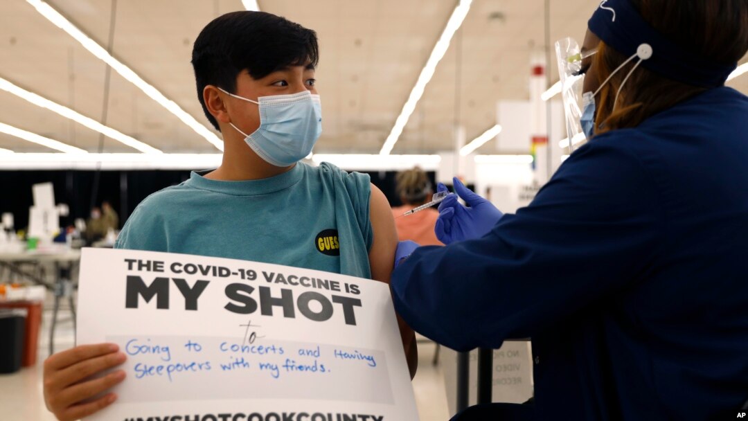 Lucas Kittikamron-Mora (13), memegang tanda untuk mendukung vaksinasi COVID-19 saat disuntik vaksin Pfizer pertamanya di Departemen Kesehatan Masyarakat Cook County, di Des Plaines, Illinois, 13 Mei 2021. 