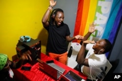 FILE - In this photo taken in Nairobi on June 11, 2020, Raymond Brian, center, a Ugandan refugee jokes with fellow LGBT refugees Chris Wasswa, left, and Kasaali Brian, right, at a makeshift studio they use for recording podcasts.