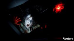 Seorang aktor dari kelompok Kowagarasetai berperan sebagai zombie sedang menakut-nakuti pengunjung dalam mobil di pertunjukan rumah hantu di Tokyo, 3 Juli 2020. (Foto: Reuters)