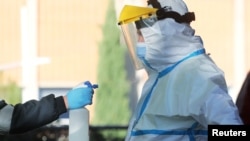 Seorang petugas mobil ambulans menerima semprotan disinfektan dari rekannya di Leganes, pinggiran Madrid, Spanyol. 