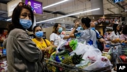 Shoppers wearing face masks with a cart full of food supplies wait in line to pay at a supermarket counter in Singapore, Tuesday, Mar. 17, 2020. (AP Photo/Ee Ming Toh)