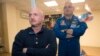 In this March 26, 2015 file photo, U.S. astronaut Scott Kelly, right, crew member of the mission to the International Space Station, stands behind glass in a quarantine room, behind his brother, Mark Kelly, also an astronaut, after a news conference (AP Photo/Dmitry Lovetsky)