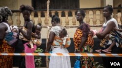 Des mères et leurs enfants font la queue pour voter dans un bureau à Freetown, en Sierra Leone, le 7 mars 2018. (VOA/Jason Patinkin)