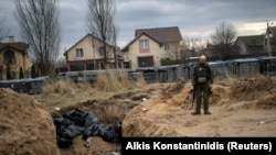 A Ukrainian soldier reacts after paying his respects next to a mass grave in Bucha. April 6, 2022. (Alkis Konstantinidis/Reuters)