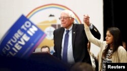 Bernie Sanders levanta la mano de una joven inmigrante durante el cabildo abierto en el casino Nación Navajo en Flagstaff, Arizona.