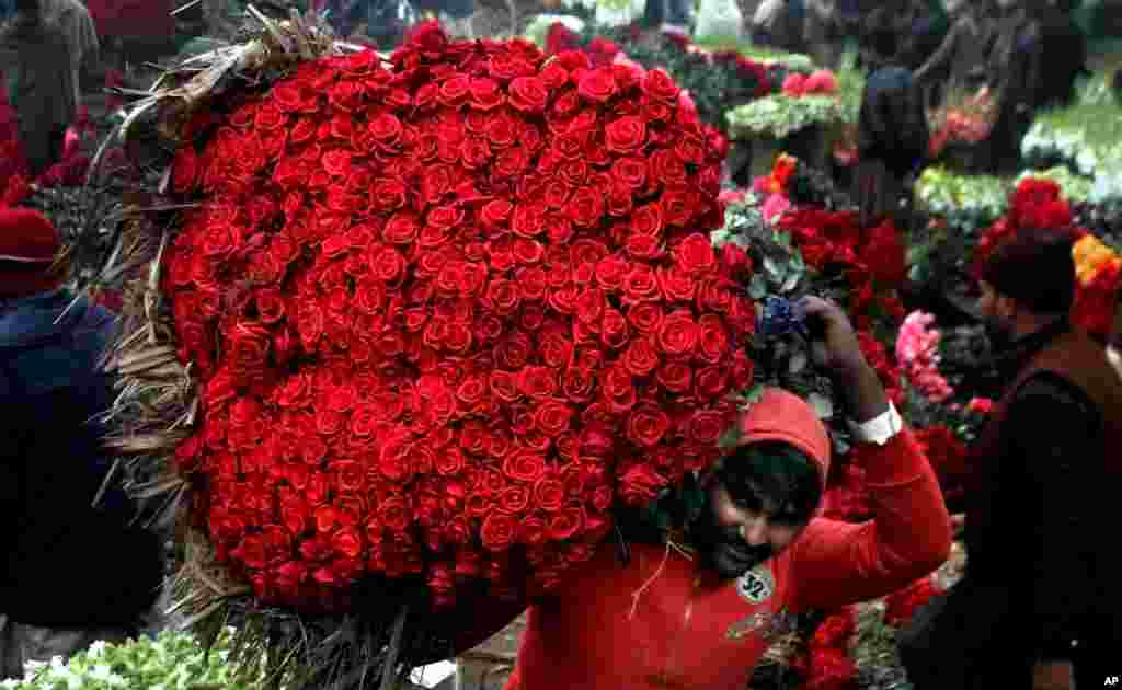 A laborer carries a bundle of red roses at a wholesale flower market in Lahore, Pakistan.