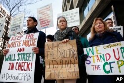 Mike Litt, left, Kaitlyn Vitez, and Ruth Susswein, gather with other members of consumer advocate groups to protest outside of the Consumer Financial Protection Bureau in Washington during a news conference with consumer groups that oppose Mick Mulvaney being named acting director for the bureau, Nov. 27, 2017.
