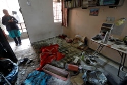 A woman stands behind the damaged belongings of students of Jawaharlal Nehru University at a hostel room after it was attacked by a mob, in New Delhi, India, Jan.6, 2020.