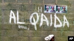 FILE - A girl walks past a wall with graffiti about the al-Qaida network in a Muslim area of the northern city of Kano, Nigeria.