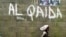 FILE - A girl walks past a wall with graffiti about the al-Qaida network in a Muslim area of the northern city of Kano, Nigeria.