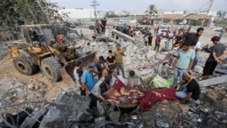 Palestinianos de pé no local de um ataque aéreo israelita, no centro da Faixa de Gaza