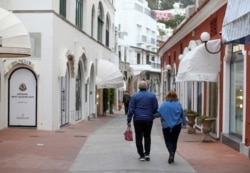 FILE - People walk in an almost deserted street, hoping for the return of foreign tourists and a busy summer season despite the coronavirus disease, on the glamorous tourist island of Capri, Italy, April 28, 2021.