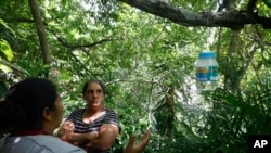 Rubenia Montoya looks at a jar containing mosquito eggs hanging from her tree as a Doctors Without Borders volunteer explains how these mosquitoes help to fight dengue, in Tegucigalpa, Honduras, Aug. 23, 2023.