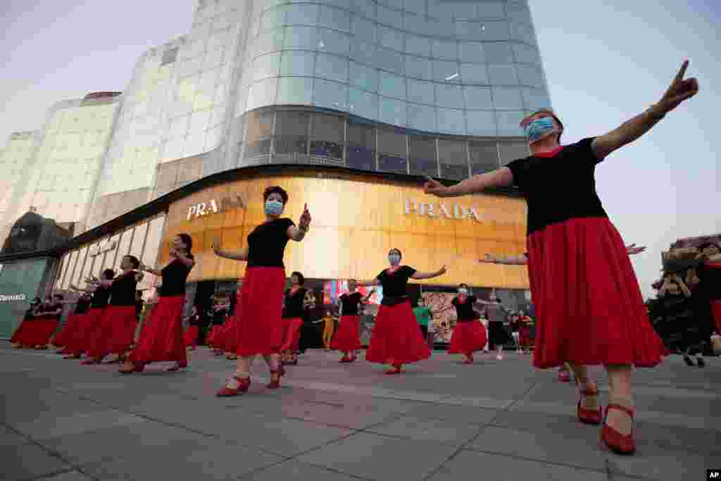 اعضای یک گروه با ماسک در حال اجرای برنامه هنری و رقص در مرکزی در شهر پکن