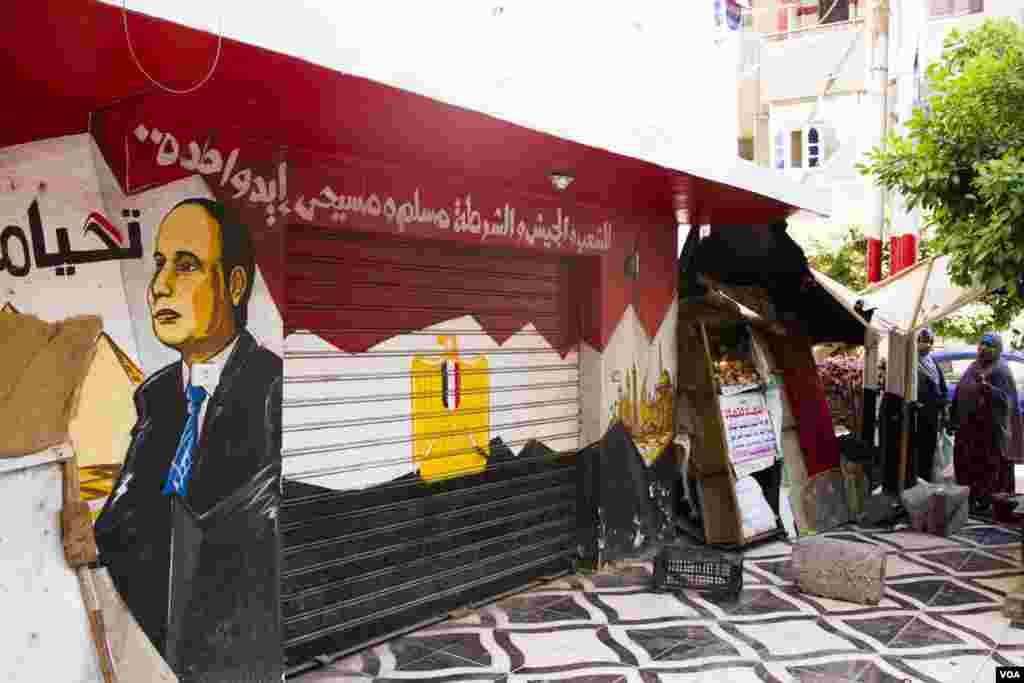 A store’s entrance in the church’s area is painted with Egyptian flag colors and president Sissi’s face and a banner reading: “The nation, military, police, Muslim and Christian are one hand,” Tanta, Egypt, Saturday, May 20, 2017. (H. Elrasam/VOA)