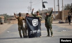 FILE - Shi'ite Popular Mobilization Forces (PMF) fighters remove an Islamic State flag after liberating the city of Al-Qaim, Iraq, Nov. 3, 2017.