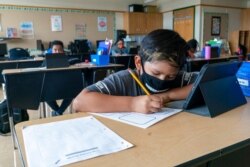 FILE - A student wears a face mask while doing work at his desk at the Post Road Elementary School, in White Plains, New York, Oct. 1, 2020.