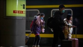 Travelers wearing face masks prepare to board their train at the Beijing West Railway Station in Beijing, Tuesday, Jan. 21, 2020.