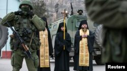 Orthodox monks pray next to armed servicemen near Russian army vehicles outside a Ukrainian border guard post in the Crimean town of Balaclava March 1, 2014.