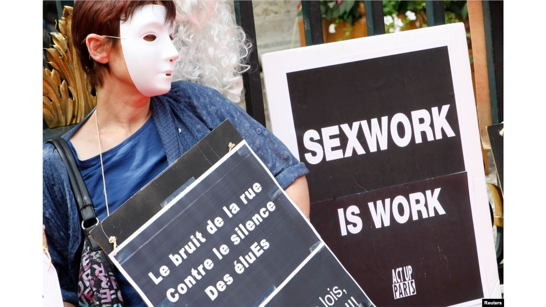 FILE - A prostitute wearing a mask holds a placard as she attends a demonstration with sex workers activists against a proposition to abolish prostitution in Lyon, France, July 6, 2012.