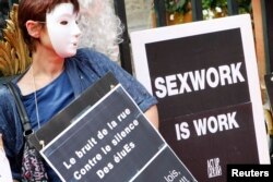 FILE - A prostitute wearing a mask holds a placard as she attends a demonstration with sex workers activists against a proposition to abolish prostitution in Lyon, France, July 6, 2012.