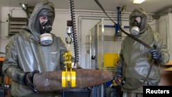 Hình minh họa - Các nhân viên mặc quần áo bảo hộ giữ một quả lựu đạn hóa học giả từ thời Thế chiến thứ hai.
