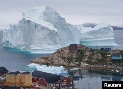A giant iceberg is seen behind an Innaarsuit settlement, Greenland, July 12, 2018.