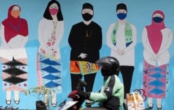 Seorang pria mengendarai sepeda motor melewati mural bertema virus corona di Jakarta, Selasa, 22 Juni 2021. (AP)