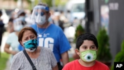 People, social distancing and wearing masks to prevent the spread of the new coronavirus, wait in line at a mask distribution event, June 26, 2020, in a COVID-19 hotspot of the Little Havana neighborhood of Miami. 