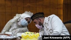 Pengantin perempuan Irra Chorina Octora asal Indonesia dan pengantin pria, Yavuz Ozdemir, dari Turki mengenakan masker di tengah kekhawatiran virus corona COVID-19, saat upacara pernikahan di Surabaya pada 25 Maret 2020.(Foto: Juni Kriswanto/AFP)