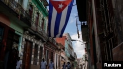 FILE - Medical students walk past a Cuban flag as they check door-to-door for people with symptoms amid concerns about the spread of the coronavirus disease (COVID-19), in downtown Havana, Cuba, May 12, 2020. 