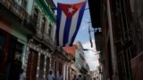 FILE - Medical students walk past a Cuban flag as they check door-to-door for people with symptoms amid concerns about the spread of the coronavirus disease (COVID-19), in downtown Havana, Cuba, May 12, 2020. 