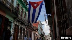 FILE - Medical students walk past a Cuban flag as they check door-to-door for people with symptoms amid concerns about the spread of the coronavirus disease (COVID-19), in downtown Havana, Cuba, May 12, 2020. 