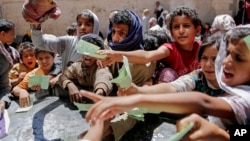 FILE - In this April 13, 2017, photo, Yemenis present documents in order to receive food rations provided by a local charity, in Sanaa, Yemen.