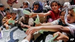 FILE - In this April 13, 2017, photo, Yemenis present documents in order to receive food rations provided by a local charity, in Sanaa, Yemen.