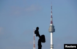 Seorang perempuan mengangkat bayinya tinggi-tinggi (tampak seperti siluet) dengan latar belakang Menara N Seoul, yang dikenal sebagai Menara Namsan, di Seoul, Korea Selatan, 2 Oktober 2018. (Kim Hong-Ji/REUTERS)