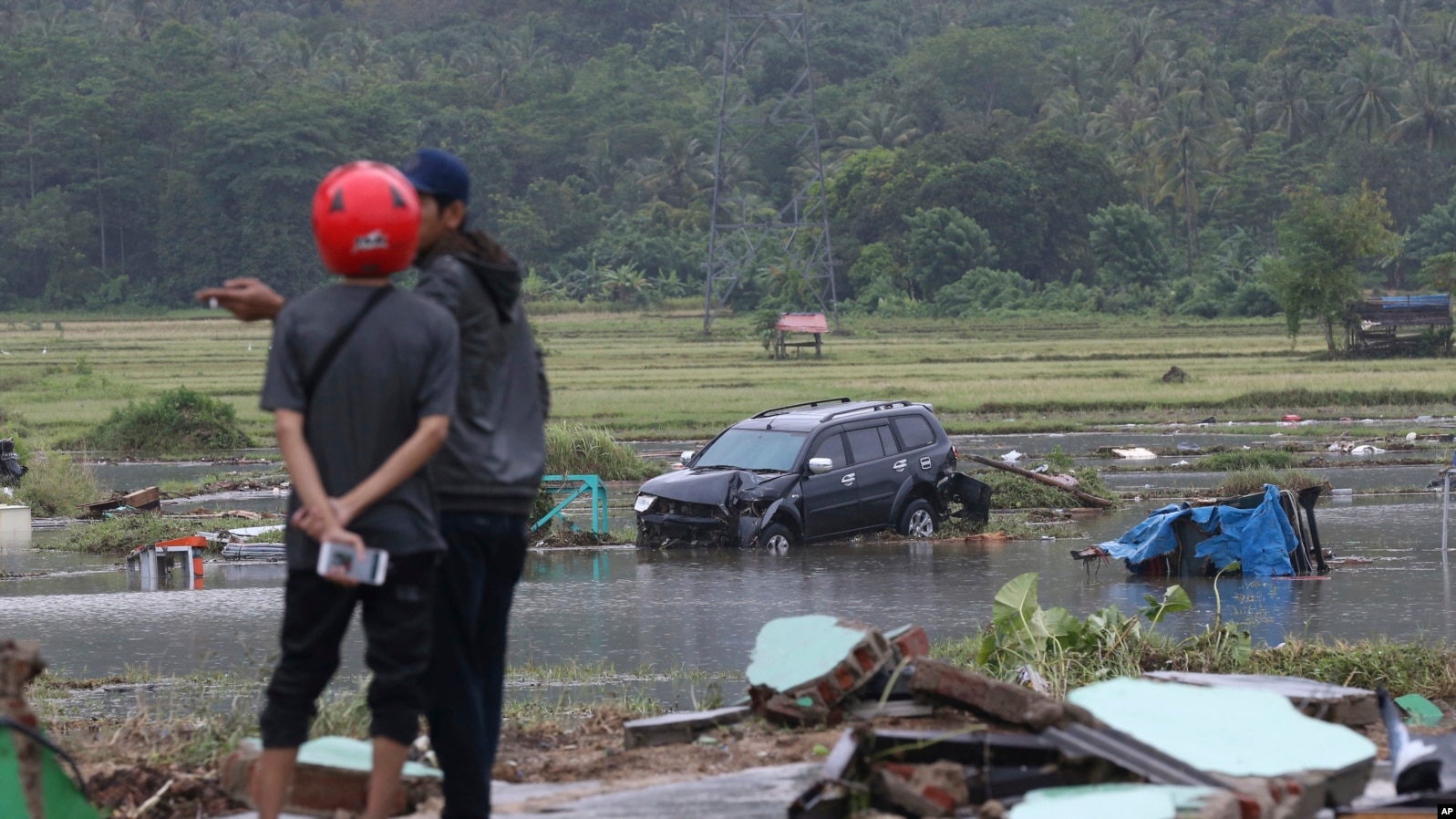 Afectados de pie cerca a un coche destruído por un tsunami en Carita, Indonesia, el 23 de diciembre del 2018