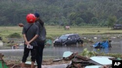 Afectados de pie cerca a un coche destruído por un tsunami en Carita, Indonesia, el 23 de diciembre del 2018