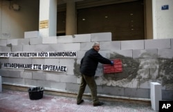 A protester works on a wall built by health workers during a demonstration outside the Health Ministry in Athens, Dec. 14, 2016. The banner reads: "Health ministry. We are closed due to memorandums. We have been transferred to Brussels."