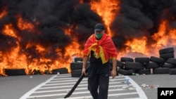 A man walks past burning tires at a barricade set up to block access roads to the historic city of Cetinje during a protest against the inauguration of the new head of the Serbian Orthodox Church on September 5, 2021 in Montenegro. - The new head of the…