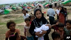 An internally displaced Rohingya woman holds her newborn baby surrounded by children in the foreground of makeshift tents at a camp for Rohingya people in Sittwe, northwestern Rakhine State, Burma, May 13, 2013.