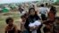 An internally displaced Rohingya woman holds her newborn baby surrounded by children in the foreground of makeshift tents at a camp for Rohingya people in Sittwe, northwestern Rakhine State, Burma, May 13, 2013.