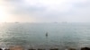 资料照片：在伊朗南部港口城市阿巴斯港外海，一名男子在海湾水域涉水，背景中可见船只正通过霍尔木兹海峡。（2026年9月7日）